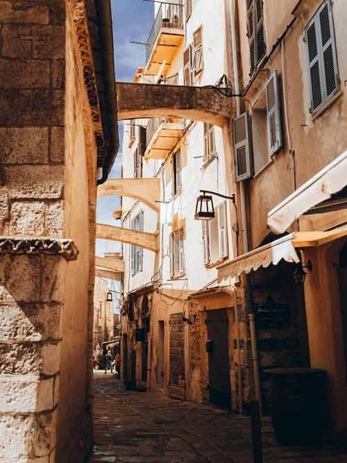 Ruelle étroite et ensoleillée de la vieille ville de Bonifacio, avec arches en pierre et façades aux volets blancs