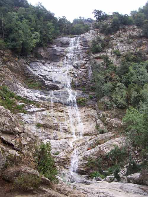 vue d'ensemble de la cascade du Voile de la Mariée en Corse, dévalant une haute paroi rocheuse entourée de végétation