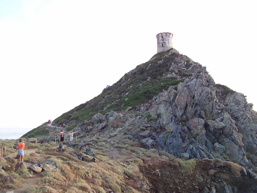 Tour génoise de la Parata perchée sur un promontoire rocheux avec des randonneurs en contrebas, près d’Ajaccio en Corse-du-Sud