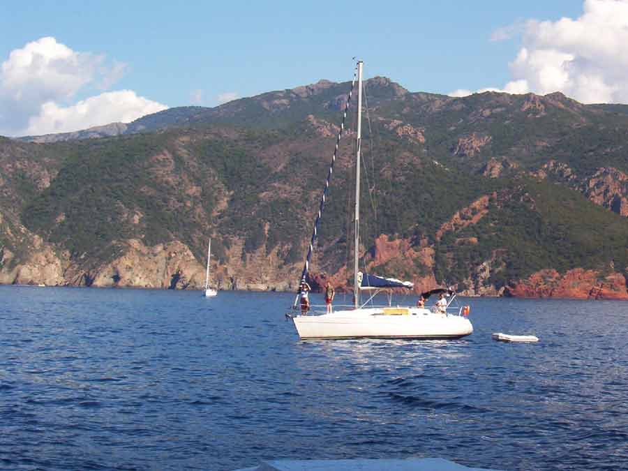 Voilier naviguant près des falaises de la réserve naturelle de Scandola en Corse