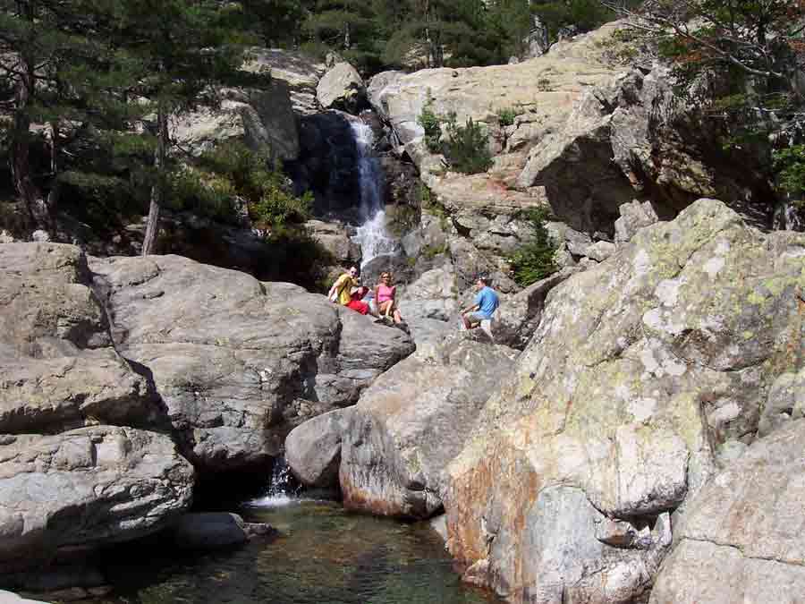 Famille assise sur les rochers près d’une vasque naturelle à la cascade des Anglais en Corse