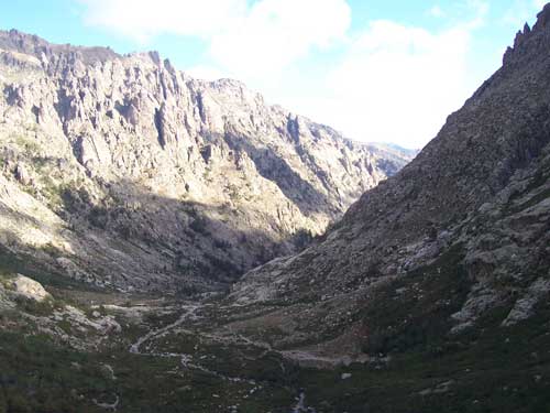 Début du sentier de randonnée dans la vallée de la Restonica vers le lac de Melo en Corse, entourée de montagnes escarpées