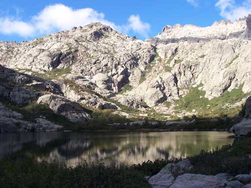 Lac Melo entouré de parois rocheuses dans la vallée de la Restonica, sous un ciel bleu en Corse