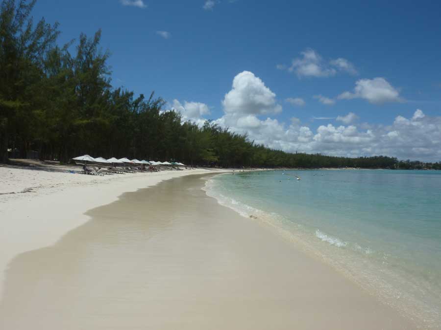 Plage paisible de Mont-Choisy avec mer calme, sable blanc et ligne de parasols à l’ombre des arbres
