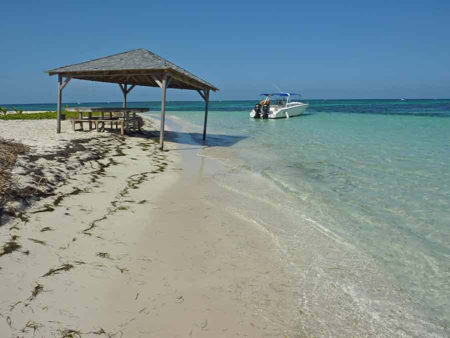 Carbet en bois sur la plage de l’îlet Caret avec bateau amarré dans le lagon turquoise