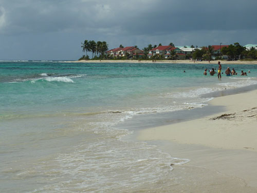 Baignade sur la plage des Raisins-Clairs à Saint-François avec vue sur les toits rouges des habitations