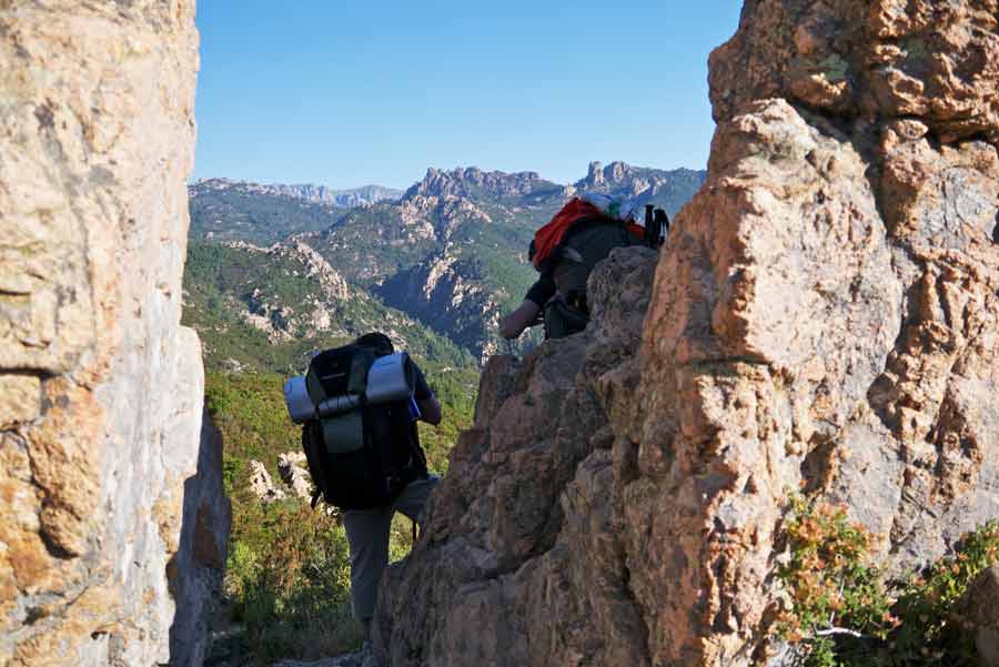 Randonneurs sur le sentier du GR20 entre Conca et Paliri, traversant un passage rocheux avec vue sur les montagnes corses