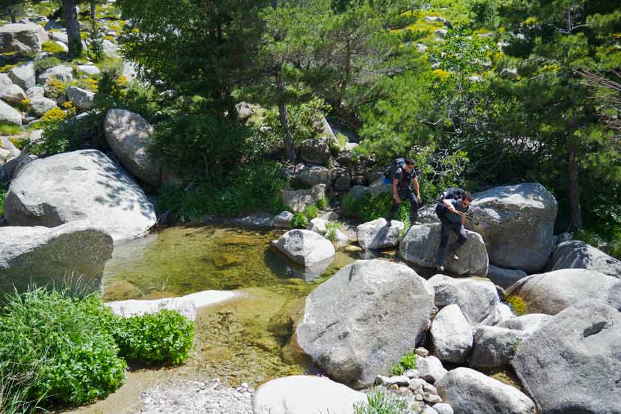 Randonneurs traversant un ruisseau sur le GR20 sud entre Bavella et Asinau, dans un décor de roches et de pins corses