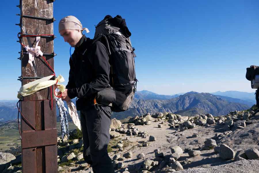 Randonneur au sommet du Monte Incudine sur le GR20 sud, face aux montagnes et au ciel bleu de Corse