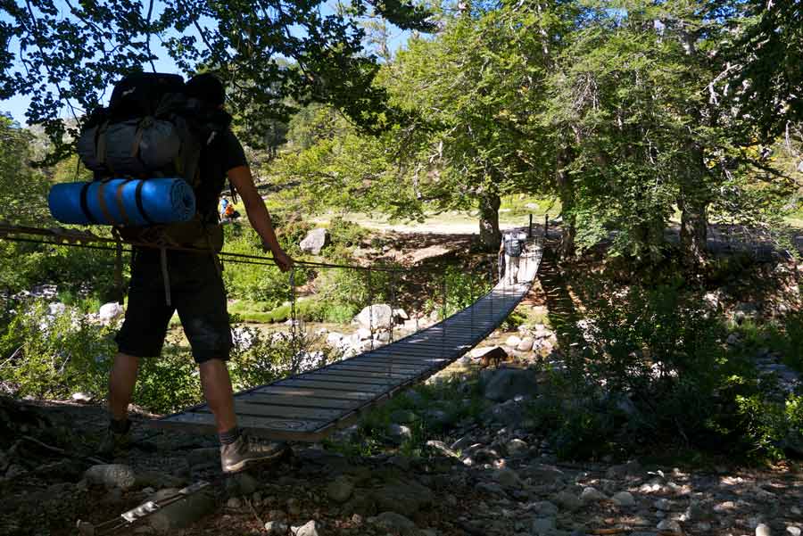 Randonneur traversant un pont suspendu sur le GR20 sud entre Asinau et Usciolu, au cœur de la forêt corse