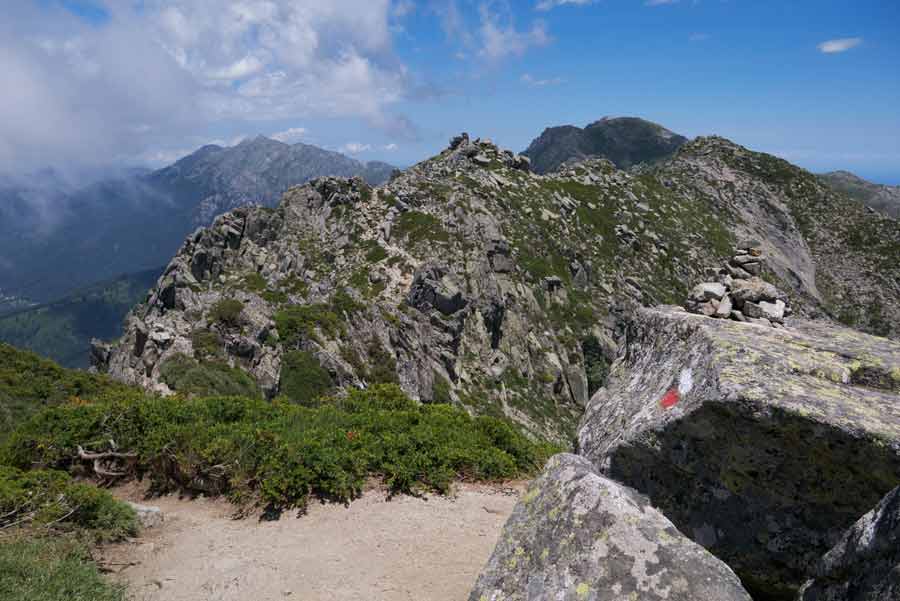 Vue panoramique sur les crêtes du GR20 sud en Corse, avec balisage rouge et blanc sur les rochers et sommets escarpés