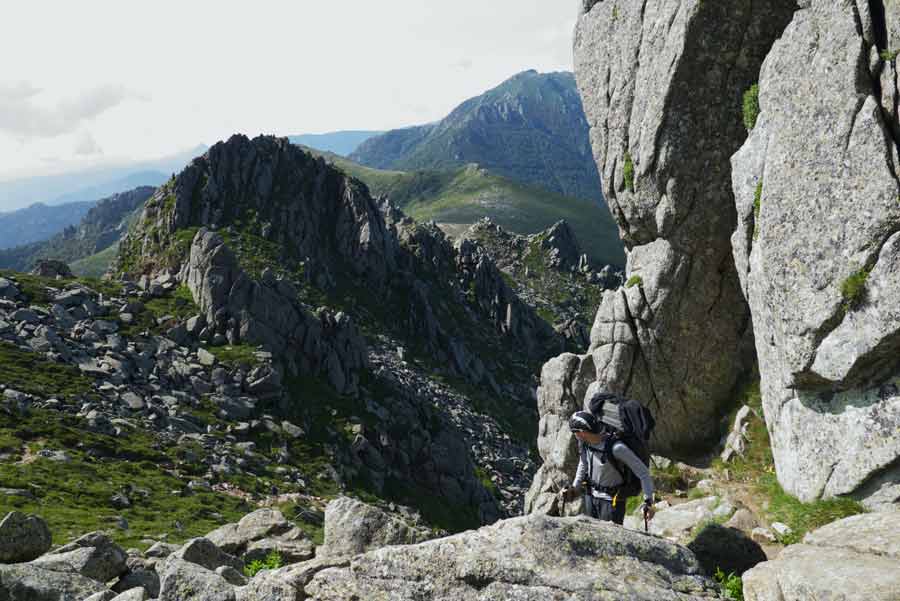 Randonneur du GR20 progressant entre les blocs de granite sur les crêtes escarpées du sud de la Corse, entre Usciolu et le col de Verde