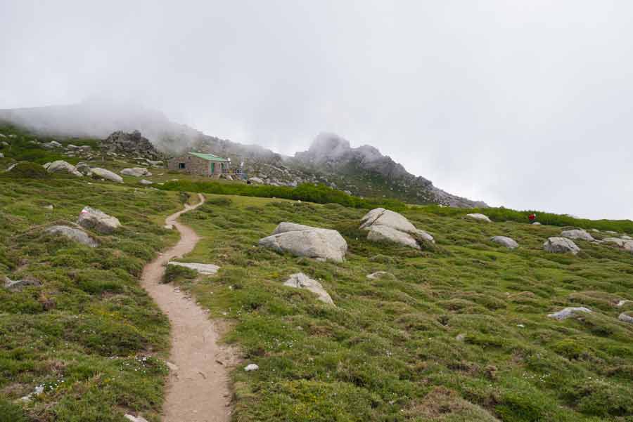 Sentier du GR20 menant au refuge de Prati sous un ciel brumeux, au cœur des montagnes verdoyantes du sud de la Corse