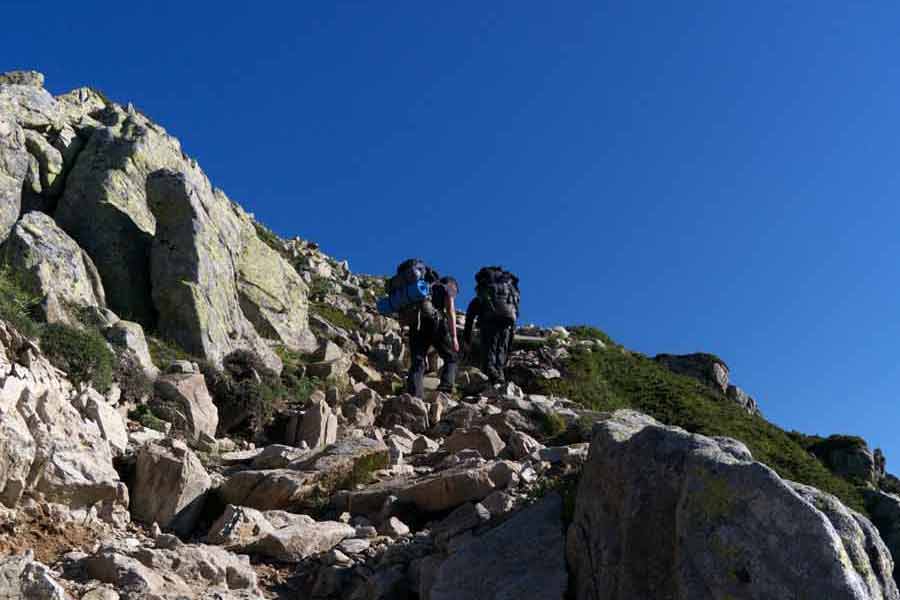 Groupe de randonneurs gravissant les pentes rocailleuses du GR20 entre L’Onda et Petra Piana, sous un ciel bleu