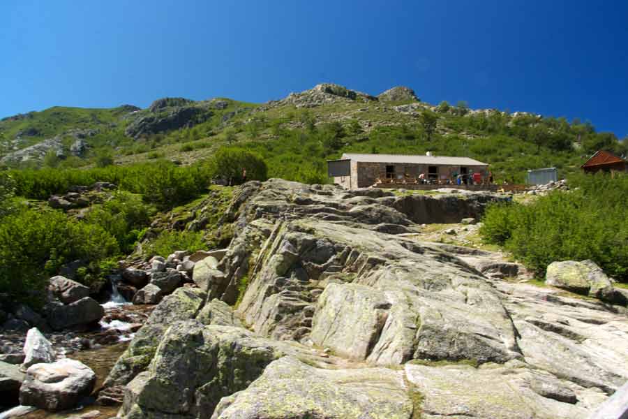 Refuge de Manganu sur le GR20 en Corse, perché au-dessus d’un ruisseau et entouré de montagnes verdoyantes