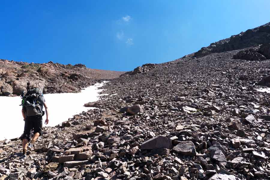 Randonneur gravissant un pierrier enneigé sur le GR20 près de Ciottulu di i Mori en Corse