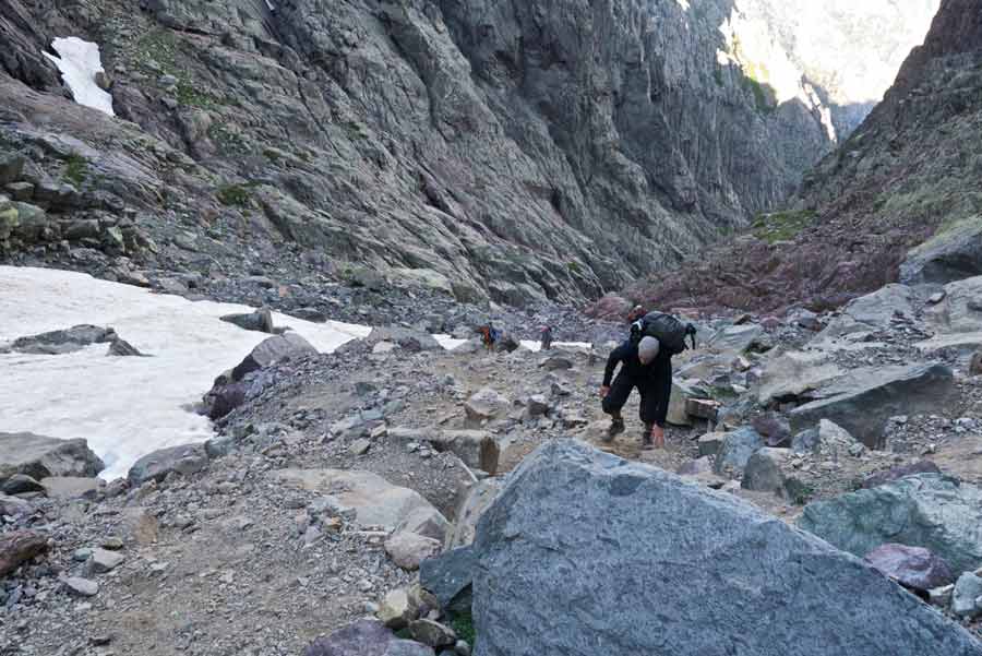 Randonneurs traversant un pierrier au cœur du cirque de la Solitude sur le GR20 en Corse