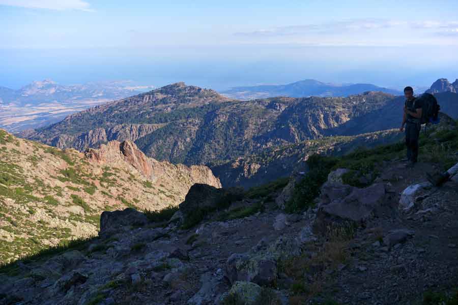 Randonneur sur le GR20 avec vue sur les montagnes corses et la mer en direction de Calvi