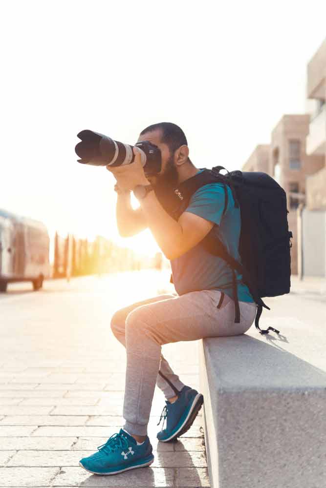 Photographe assis en ville, capturant une scène à la lumière dorée avec un téléobjectif lors d’un séjour photo