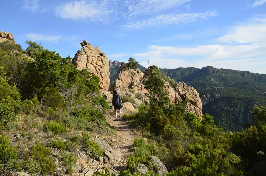 Randonneur sur un sentier en montagne en Corse avec rochers et végétation