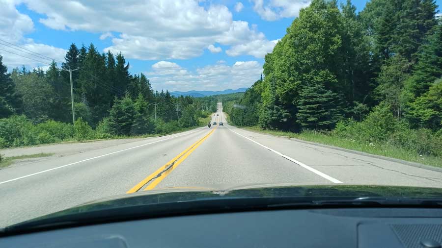 Route bordée de forêts et de montagnes en arrière-plan, vue depuis le pare-brise lors d'un road trip en amoureux