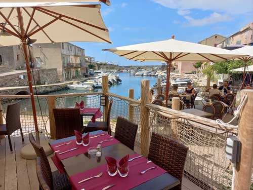 Une terrasse de restaurant les pieds dans l'eau à Centuri, face aux barques de pêcheurs amarrées