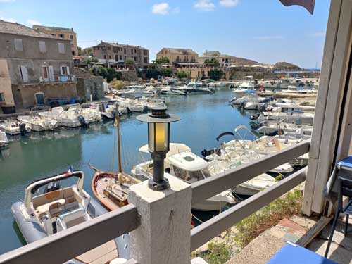 Le port de Centuri et sa flottille de bateaux de pêche, vu depuis une terrasse sous un ciel bleu