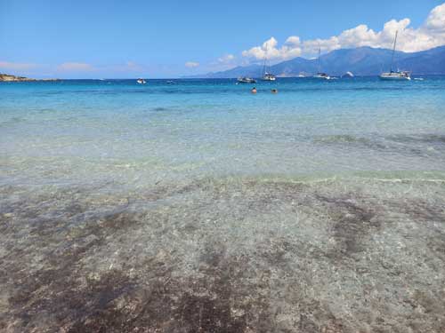 L'eau limpide de la plage de Lodo, avec voiliers au mouillage et montagnes corses en toile de fond