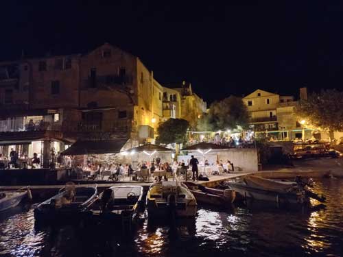 Le port d'Erbalunga animé à la nuit tombée, terrasses éclairées et barques amarrées