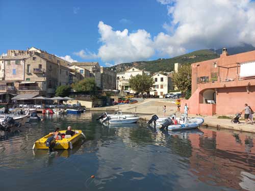 Le port d'Erbalunga animé, barques amarrées et façades colorées avec les montagnes du Cap Corse en toile de fond