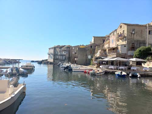 Les maisons ocre d'Erbalunga plongeant leurs fondations dans l'eau du port, bordées de terrasses de restaurants