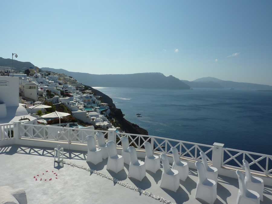 Terrasse de mariage avec chaises blanches surplombant la caldeira de Santorin en Grèce, maisons cycladiques et mer Égée en arrière-plan
