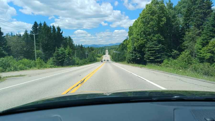 Route panoramique bordée de forêts denses au Canada, vue depuis le pare-brise vers les montagnes
