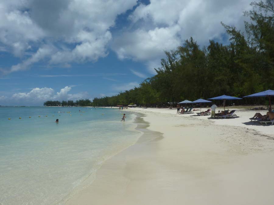 Plage de sable blanc à l'île Maurice, eau turquoise peu profonde et parasols bleus, ambiance détente pour un voyage de noces balnéaire