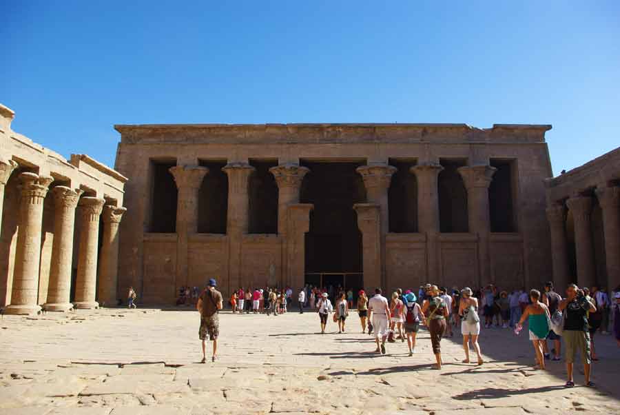 Groupe de voyageurs en circuit organisé en Égypte traversant la cour du temple d'Edfou, face à la façade à colonnes de la salle hypostyle