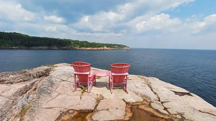 Deux chaises rouges face au Saint-Laurent sur les rochers du Centre de découverte du milieu marin des Escoumins, une halte improvisée lors de notre road trip au Québec