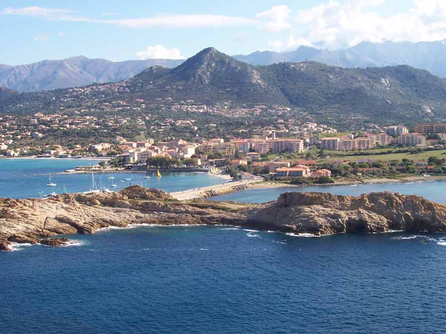 Vue sur L'Île-Rousse depuis les rochers rouges de l'île de la Pietra, avec la ville, son port et les montagnes de Balagne en arrière-plan