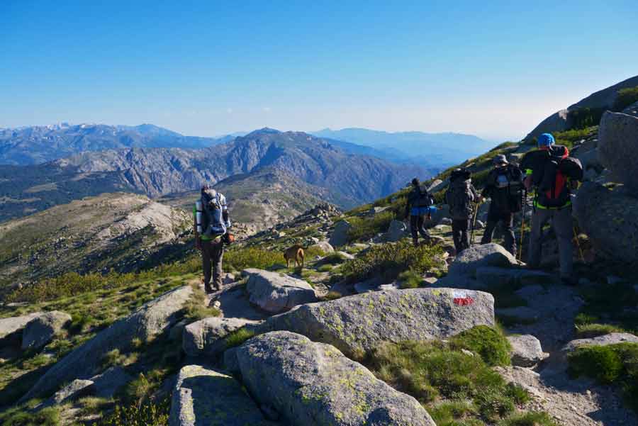 Randonneurs avec leur sac à dos sur un sentier balisé du GR20 en Corse, face aux montagnes